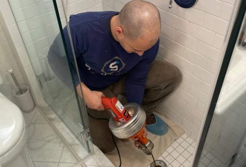 Professional plumber using drain cleaning equipment in bathroom